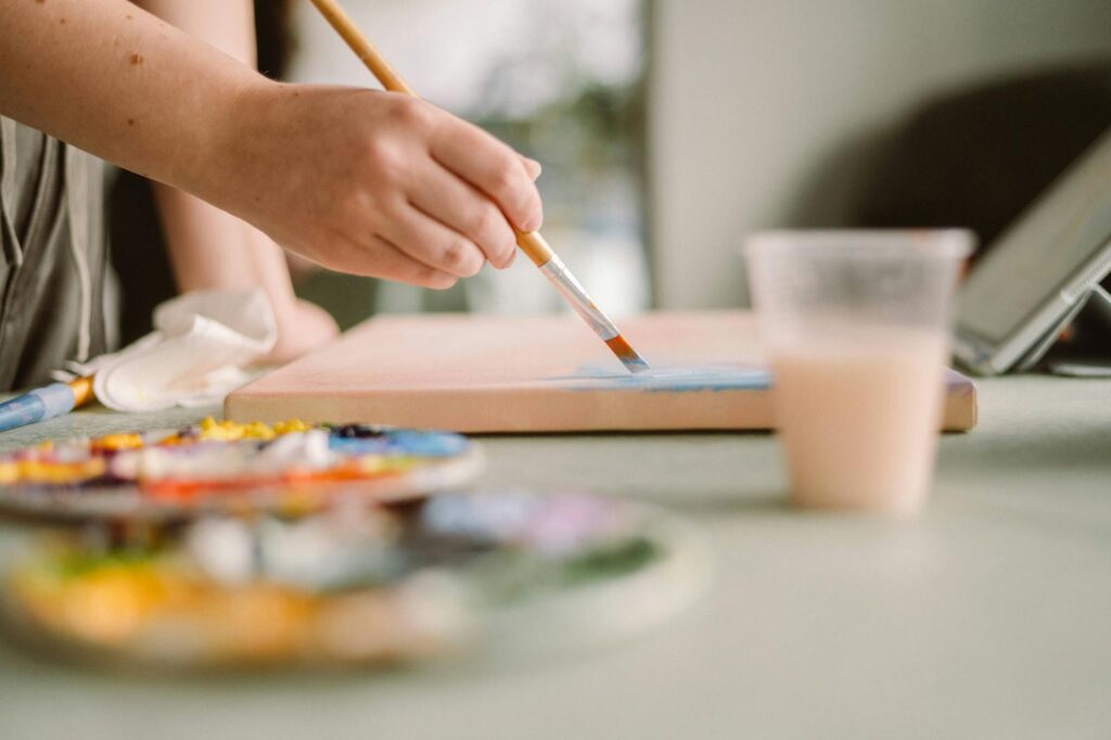 Artist applying blue paint on canvas in a sunlit home studio. Creative workspace ambiance.